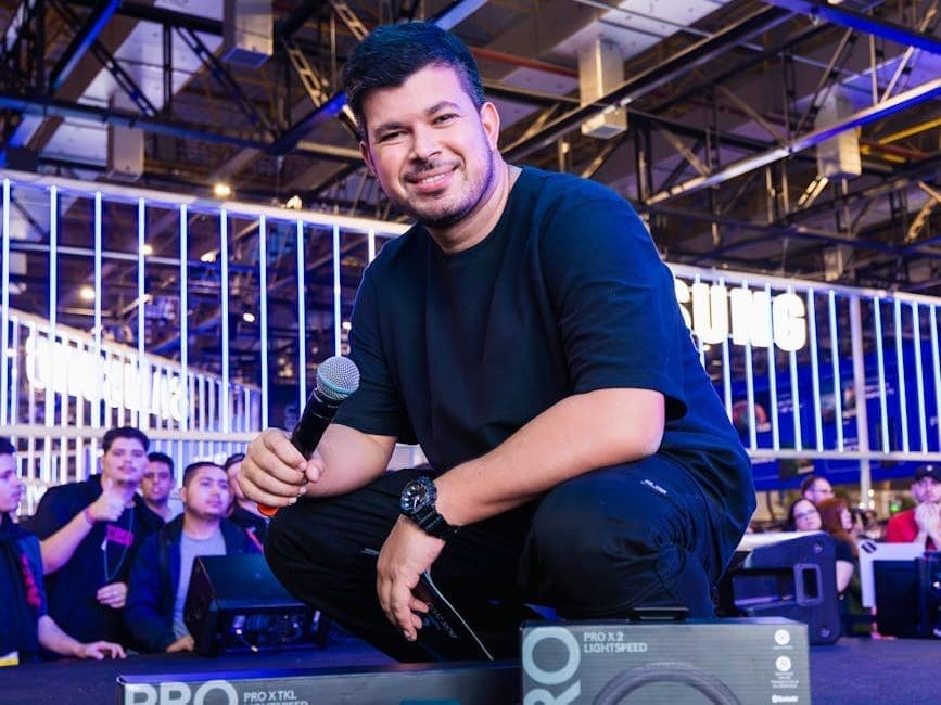 man with a microphone next to boxes with logitech gaming peripherals at computer fair