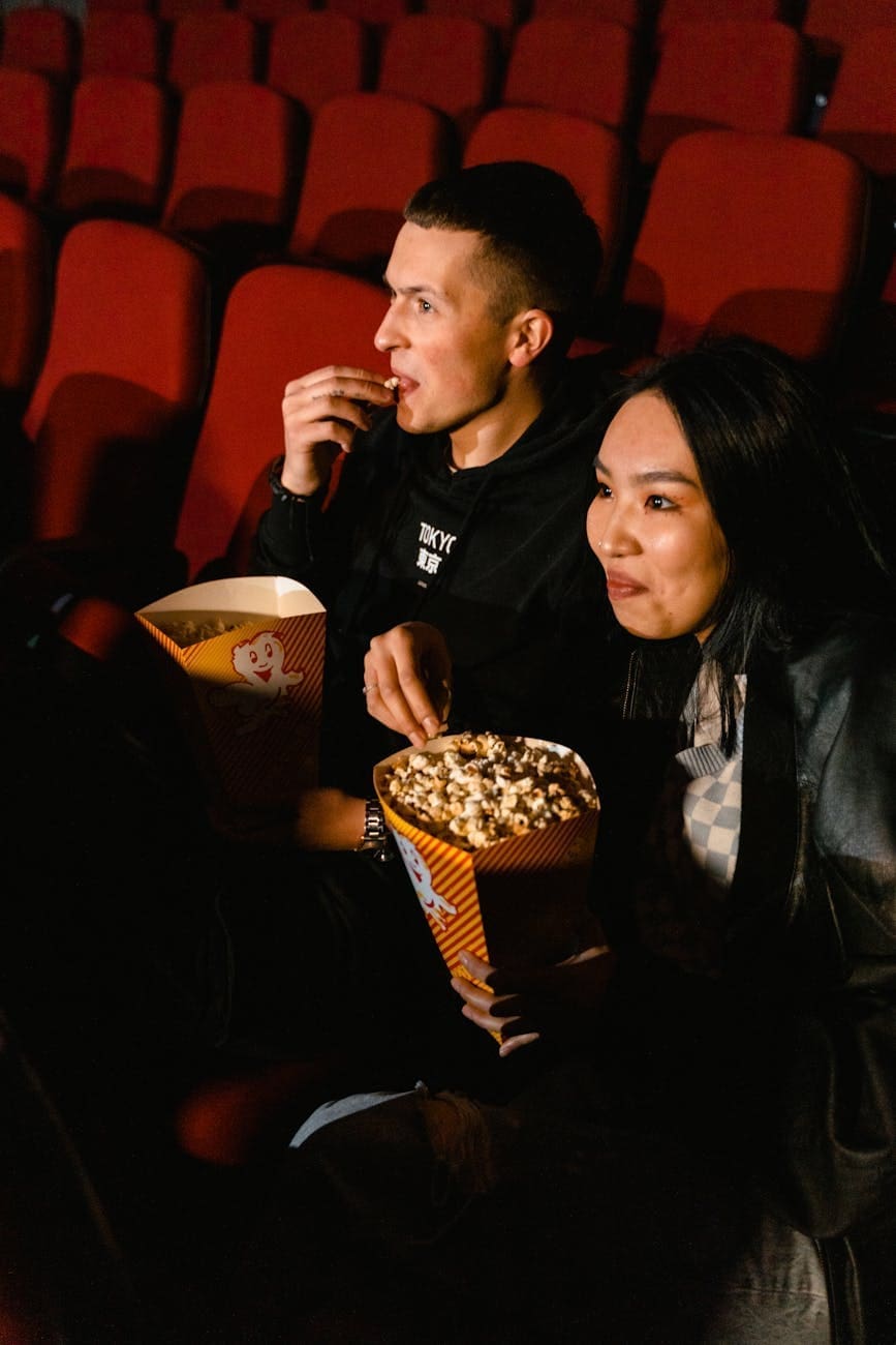 man and woman eating popcorn while sitting in a cinema