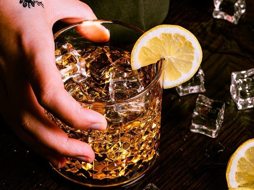 a hand holding a glass of whiskey with lemon slices