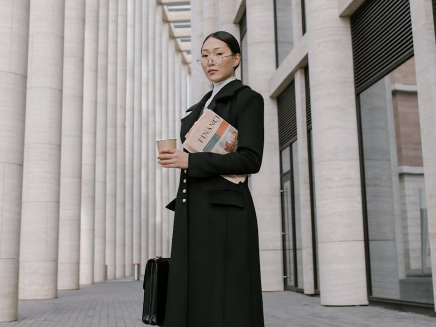 woman in black coat holding newspaper and coffee to go