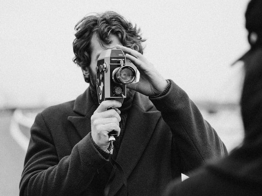 gray scale photo of man holding analog camera