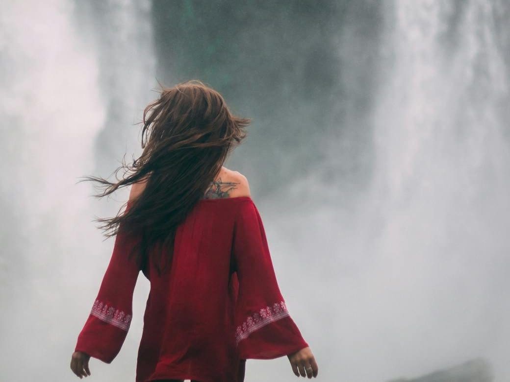 woman in red dress standing near waterfalls
