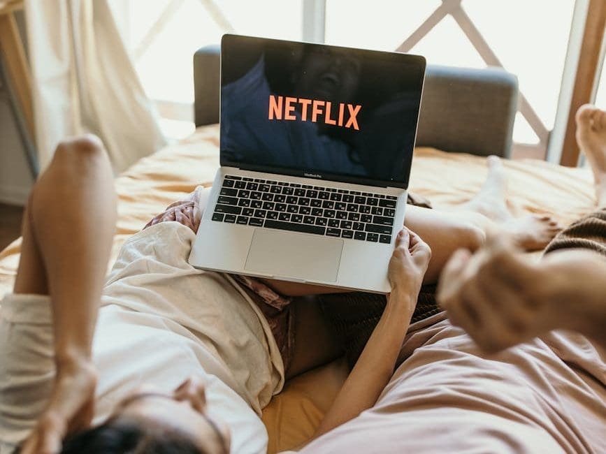 a couple lying on bed watching netflix on laptop