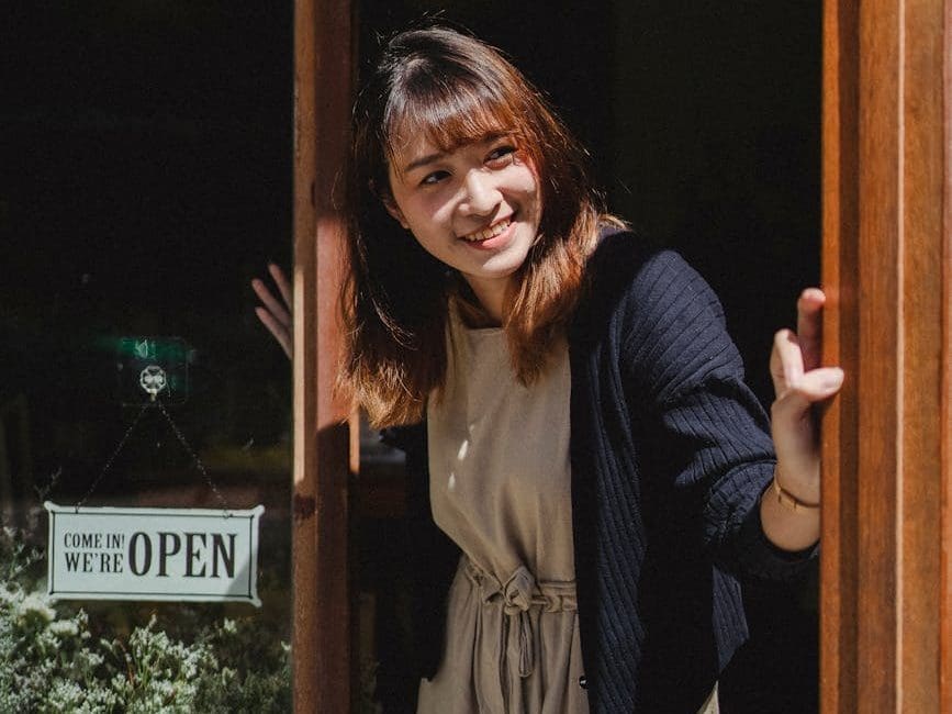 smiling asian woman in apron opening store door