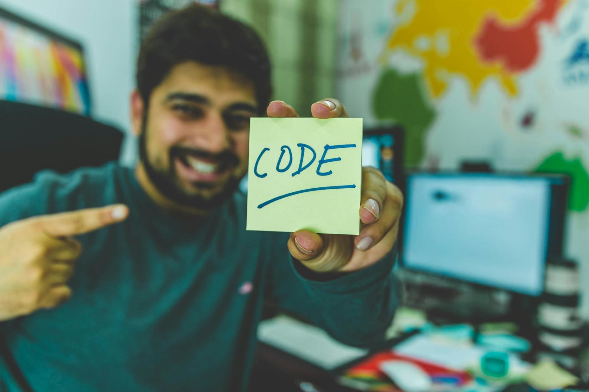 man in grey sweater holding yellow sticky note