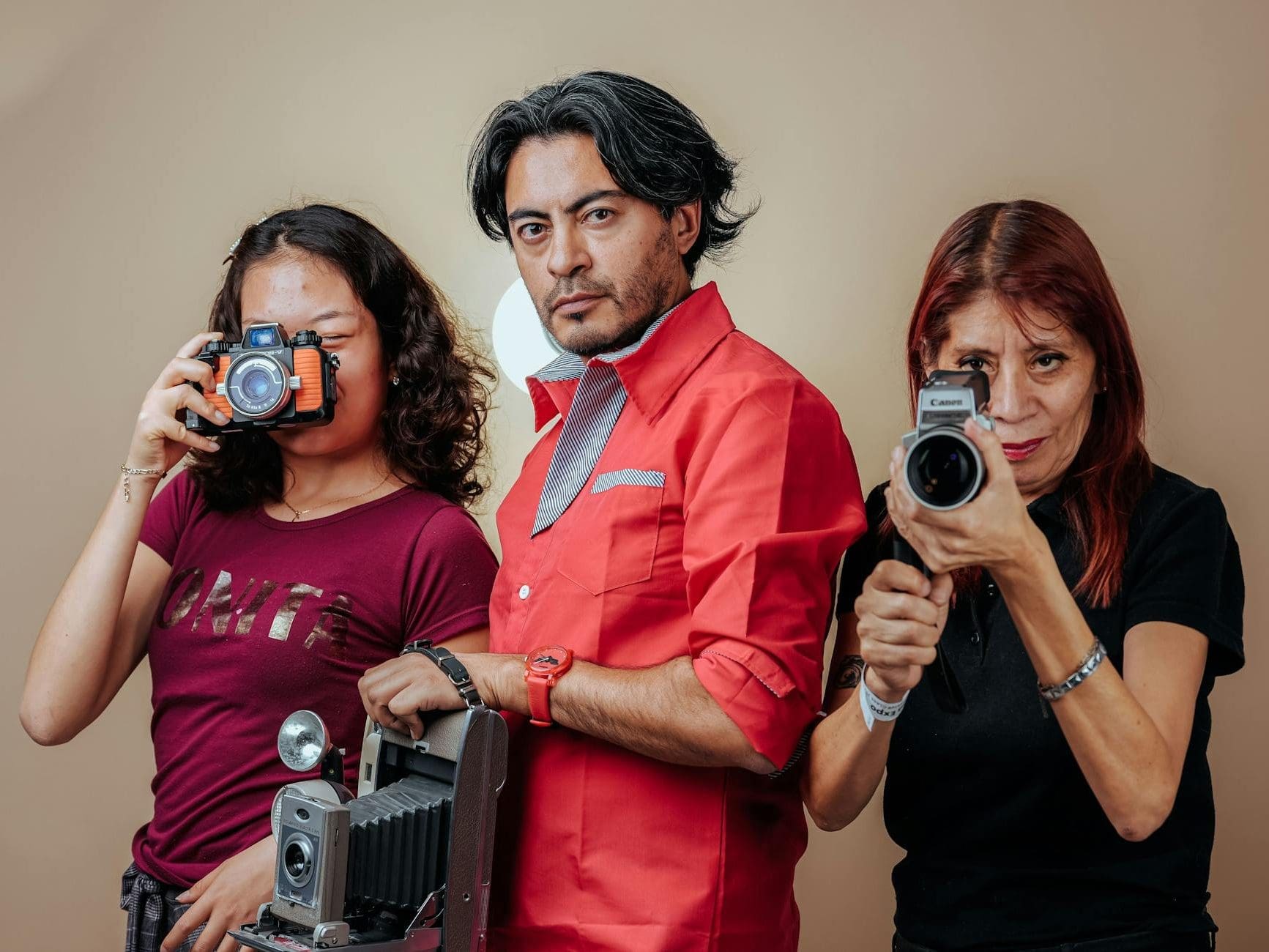 photo of two women and a man with vintage photographic equipment posing against a beige background